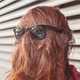Image: dark sunglasses perched on the back of a woman's head so that it looks as though her face is covered in long red hair.