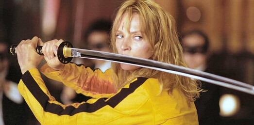 A movie still of The Bride in the Tarrantino Movie, Kill Bill holding a samurai sword above her head